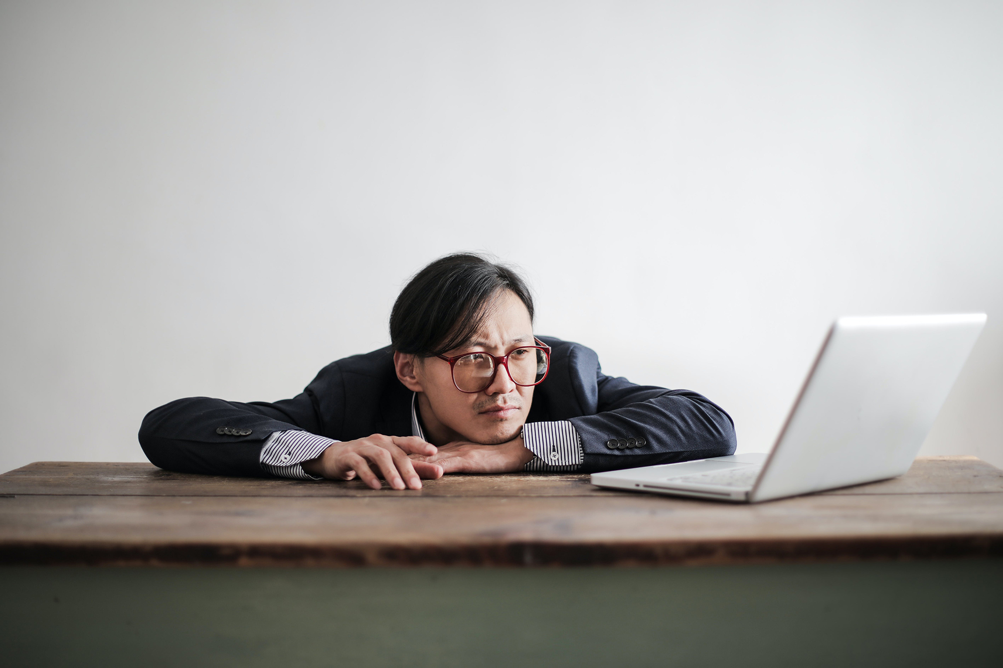 Bored man slumped on a desk in front of a laptop