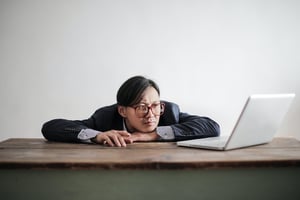 Bored man slumped at a desk in front of a laptop